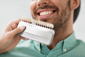 A man in a teal shirt is comparing his teeth to reference veneers for a restorative dentistry treatment.