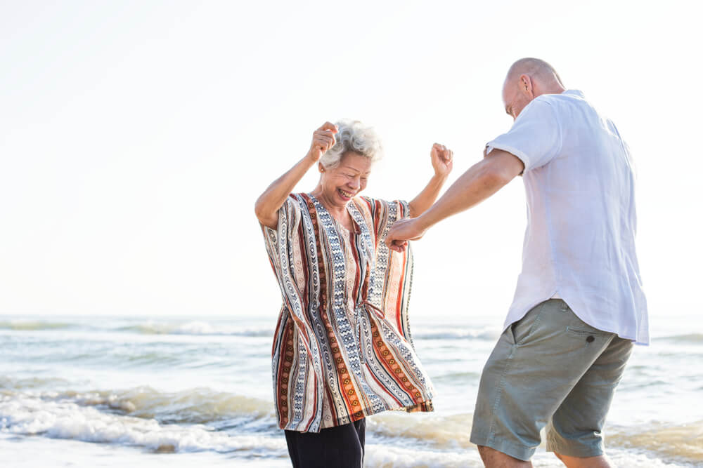 A man and woman visit the beach after their dental appointment. They're dancing and not in pain.