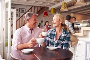 Couple enjoying coffee at a cozy café, smiling and engaging in conversation, reflecting the joy of dining out with restored confidence from dental implants.