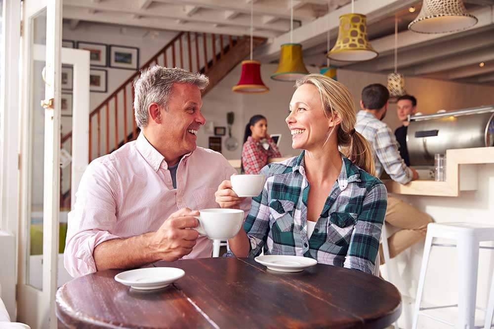 A man and woman are on a date at a coffee shop. They're smiles are beautiful thanks to restorative dentistry.