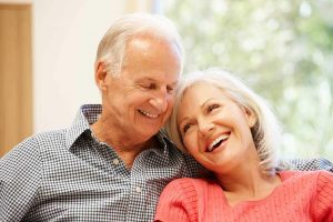 An older couple is smiling and leaning on each other. Their restorative dentistry looks beautiful.