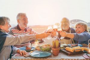 Two older couples are smiling proudly and eating dinner thanks to dental implants.