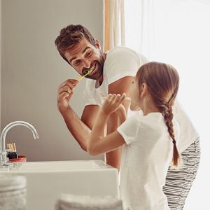 Father and daughter brushing teeth together at a bathroom sink, emphasizing dental care and fluoride treatment benefits.