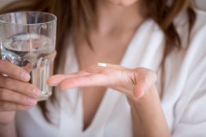 woman holding a pill and a glass of water