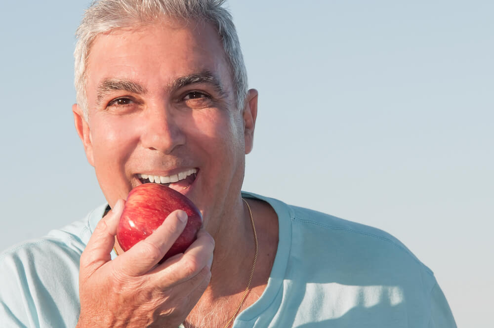 A man is eating an apple. He has stunning teeth from visiting his dentist.