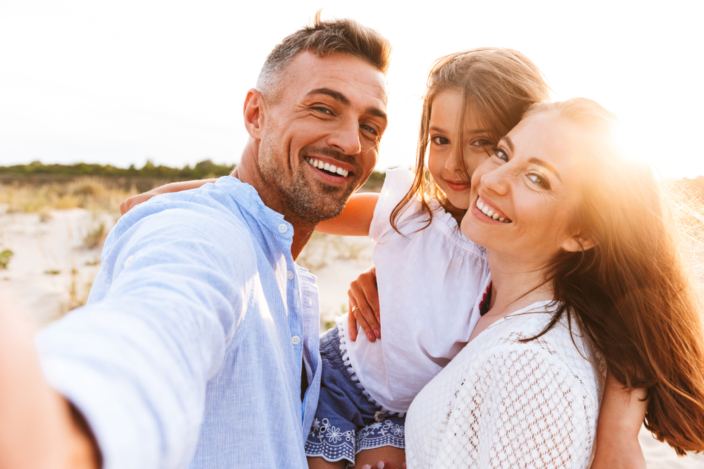 A family is on the beach and smiling proudly thanks to restorative dentistry.