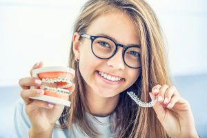 woman holding invisalign and model of teeth with braces