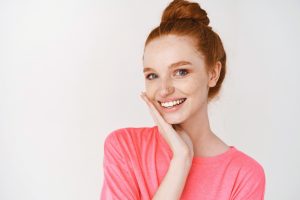 A woman is smiling with her hand to her face after visiting her dentist.