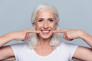 A woman points to her dental implants and smiles.